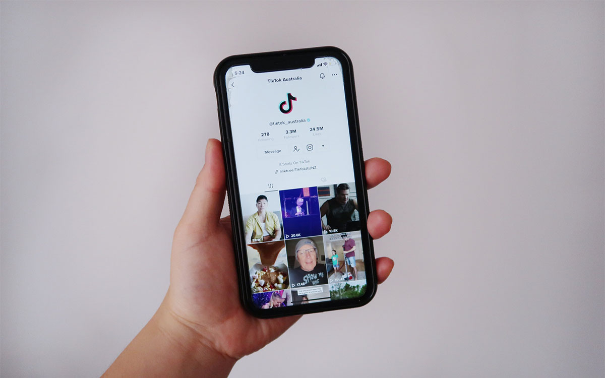A hand holds a smartphone that displays a TikTok Homepage